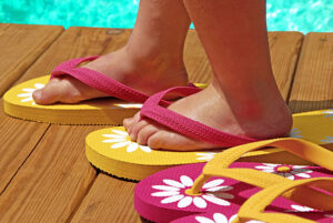 child trying on flipflops on deck next to pool